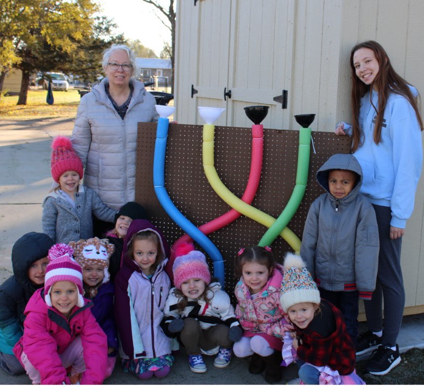 Rosalie Wehlander created an outdoor water toy with funnels, pool noodles and pails as a 4-H project. She donated it to the Iroquois Preschool for their outdoor classroom.  Pictured are Motley Barth, kneeling left, Isabelle Rose, Lanna Houghtaling, Ella Strickler, Savannah Driggers, Kaebrey Brown, Finly Dunsworth, Rowena Guthmiller. Raea Guthmiller, standing left, Mary Wienbar (preschool teacher) Carlos Perez Torres, Rosalie Wehlander.