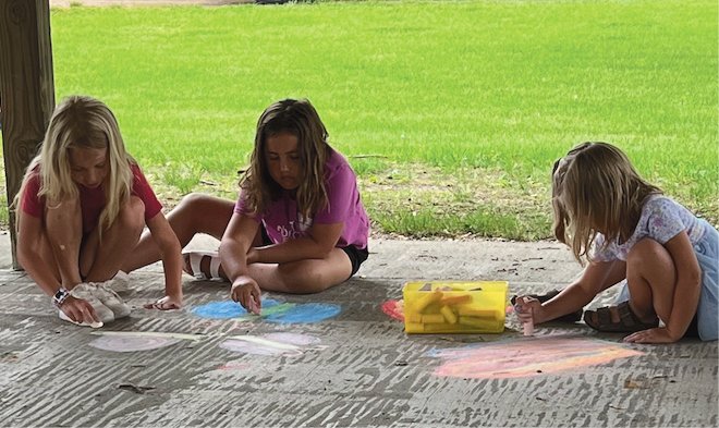 Charlee DeKnikker, left, and Madi and Veda Casper enjoy the shade under the canopy while drawing some chalk pictures during the fun night.